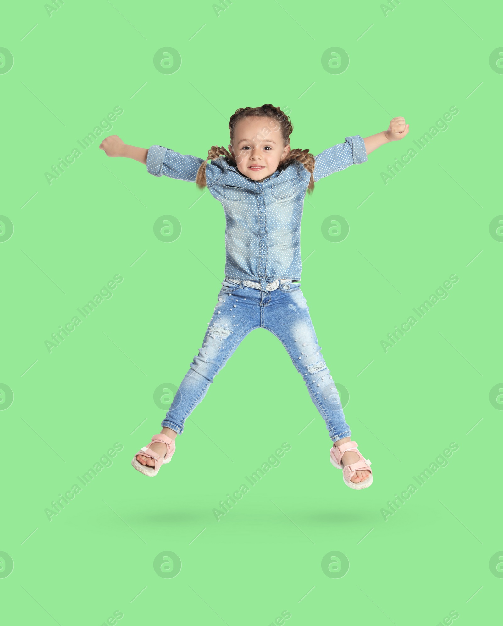 Image of Happy cute girl jumping on light green background