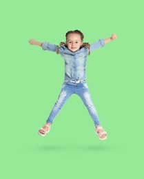 Happy cute girl jumping on light green background