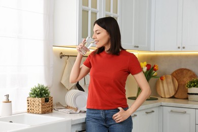 Young woman drinking fresh water in kitchen