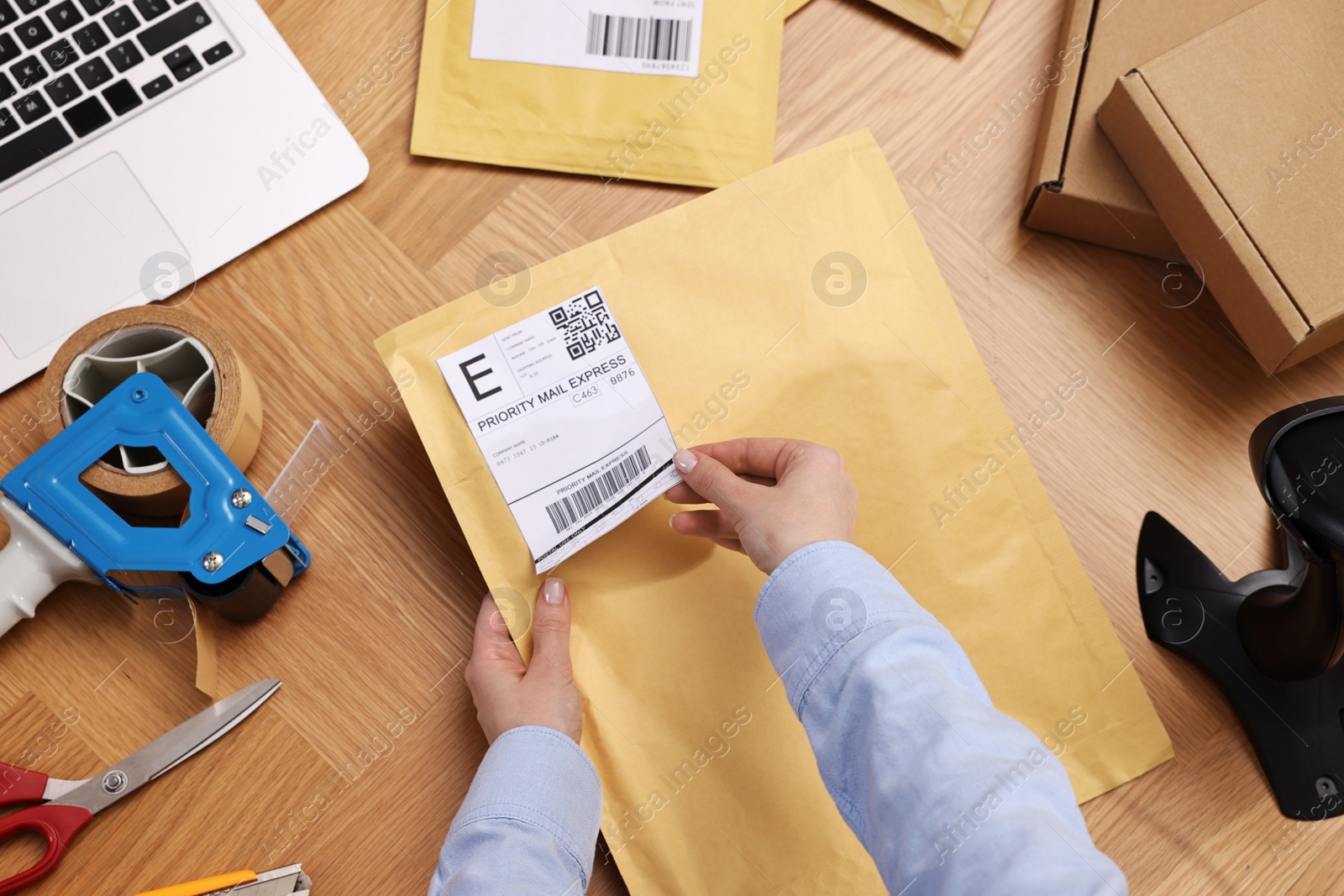 Photo of Parcel packing. Post office worker sticking barcode on bag at wooden table, top view