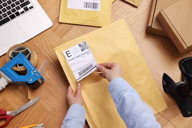 Photo of Parcel packing. Post office worker sticking barcode on bag at wooden table, top view