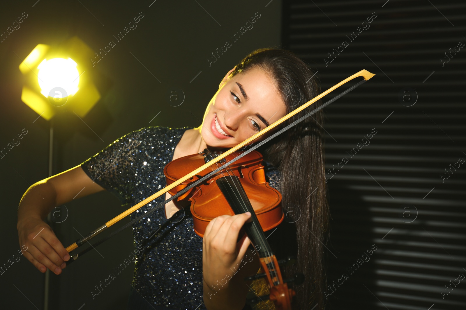 Photo of Beautiful young woman playing violin in dark room