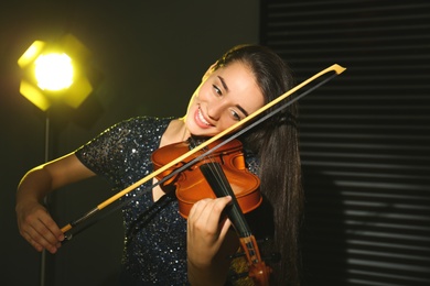 Beautiful young woman playing violin in dark room