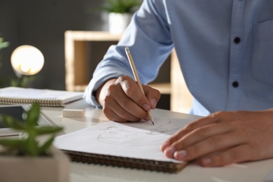 Photo of Man drawing portrait with pencil in notepad at table, closeup
