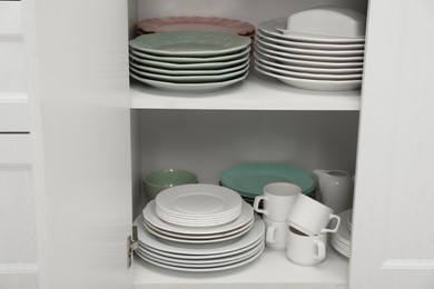 Clean plates and other crockery on shelves in cabinet indoors