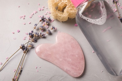 Photo of Rose quartz gua sha tool, dried lavender flowers and cosmetic product on grey table, closeup
