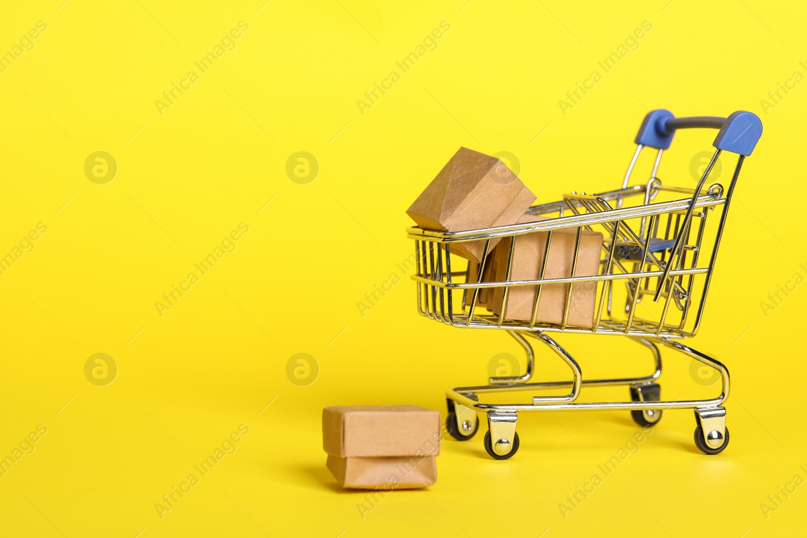 Photo of Small metal shopping cart with boxes on yellow background. Space for text