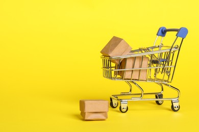Photo of Small metal shopping cart with boxes on yellow background. Space for text