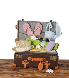 Open vintage suitcase with different beach objects packed for summer vacation on wooden table against white background