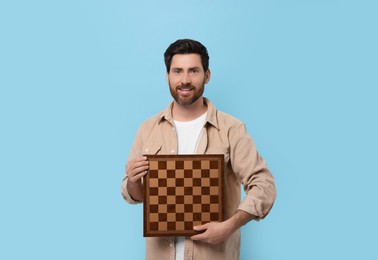 Smiling man holding chessboard on light blue background
