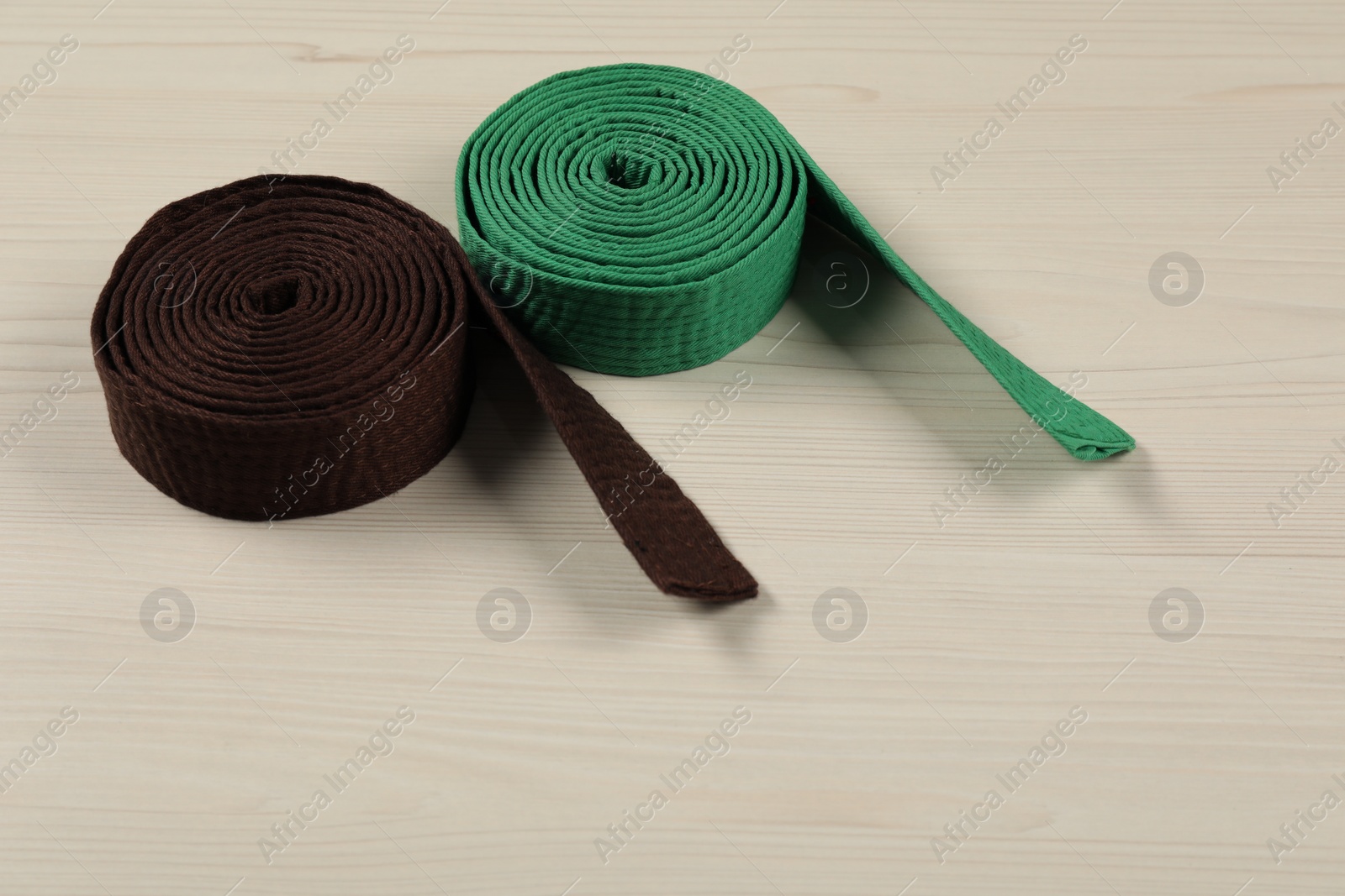 Photo of Green and brown karate belts on wooden background, space for text