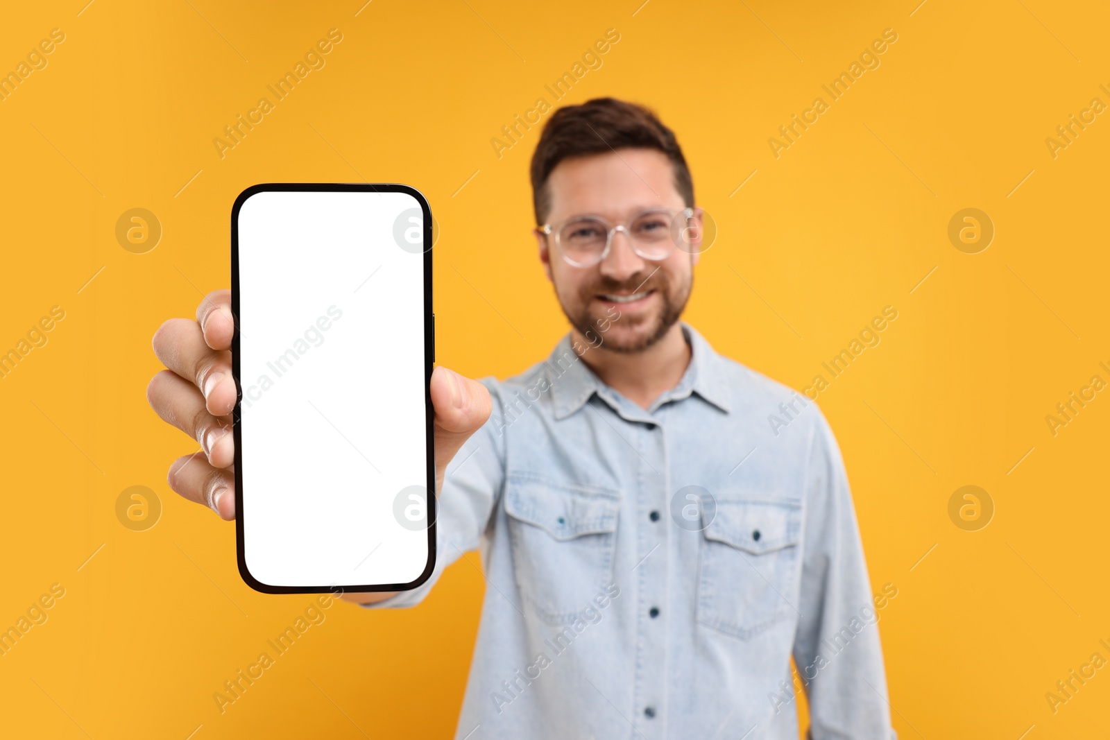Photo of Handsome man showing smartphone in hand on yellow background, selective focus. Mockup for design