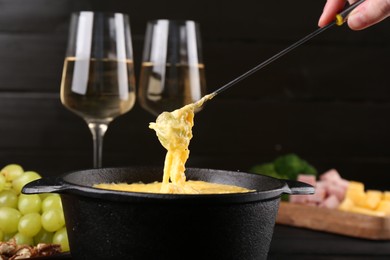 Photo of Woman dipping grape into fondue pot with melted cheese at table, closeup