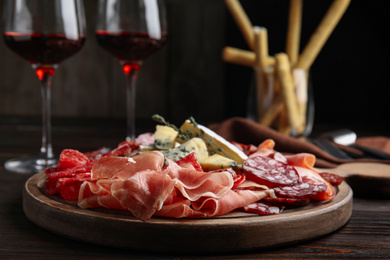 Photo of Tasty prosciutto with other delicacies served on wooden table, closeup