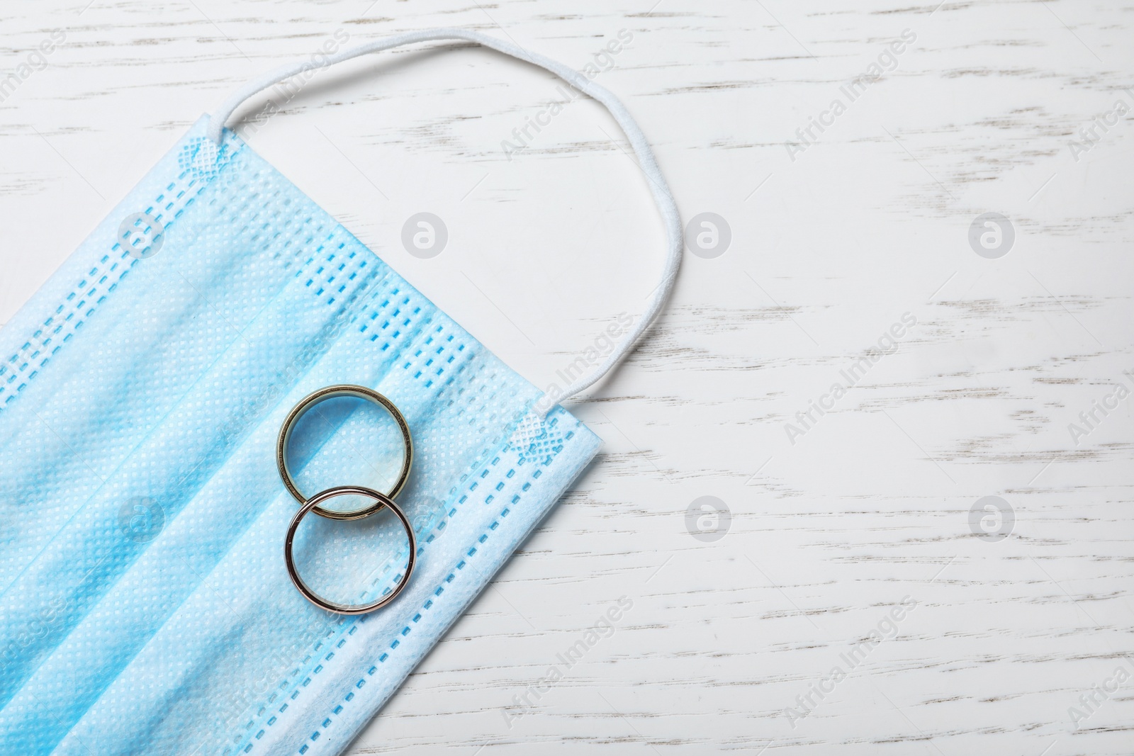 Photo of Protective mask and wedding rings on white wooden table, flat lay with space for text. Divorce during coronavirus quarantine