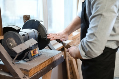 Photo of Working man using grinding machine at carpentry shop, closeup