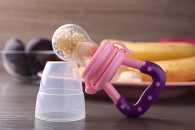 Nibbler with fresh banana on wooden table, closeup. Baby feeder