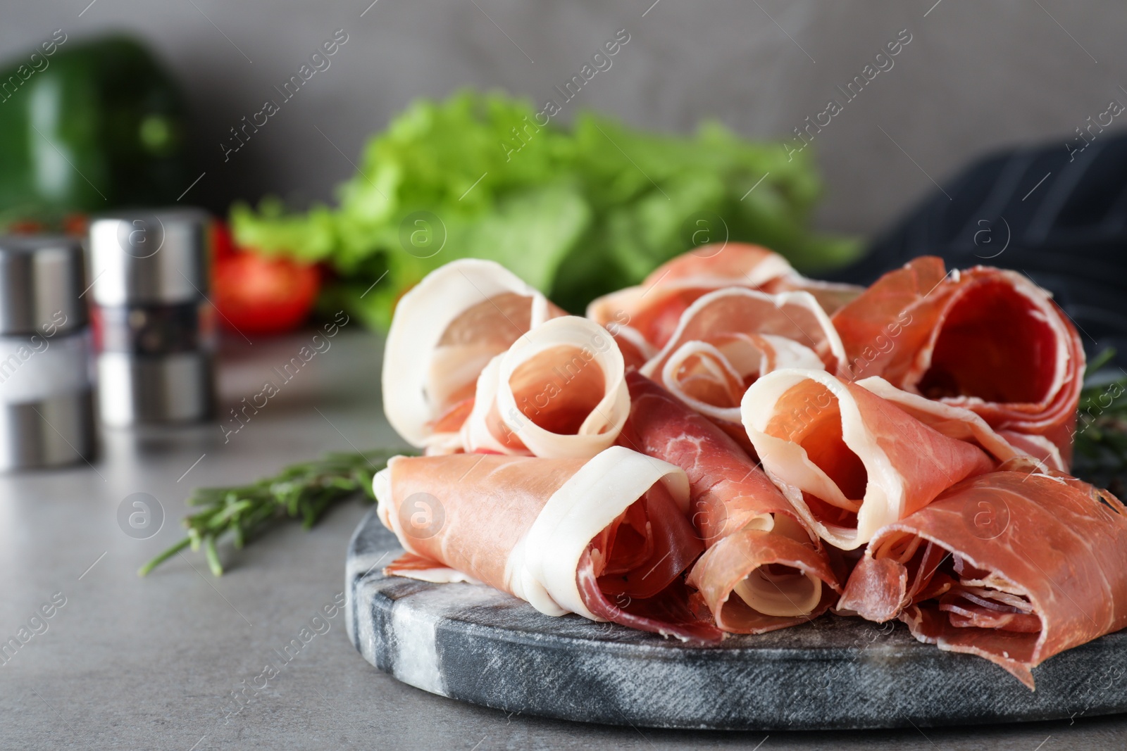 Photo of Pile of tasty prosciutto on light grey table, closeup