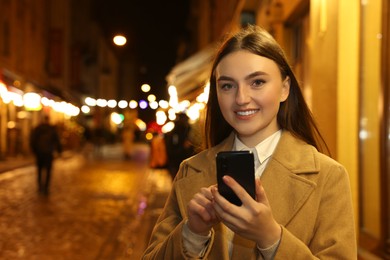 Smiling woman using smartphone on night city street. Space for text