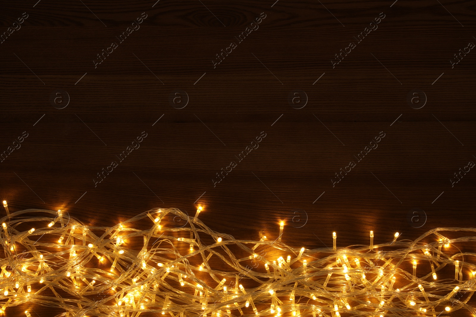 Photo of Beautiful glowing Christmas lights on wooden table, top view. Space for text