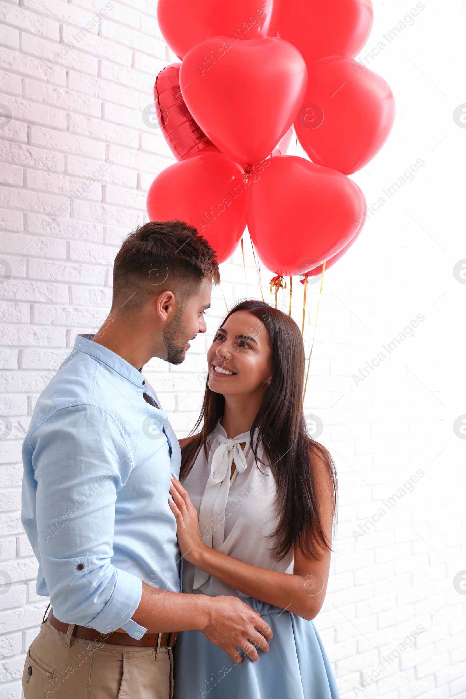 Photo of Young couple with air balloons near white brick wall. Celebration of Saint Valentine's Day