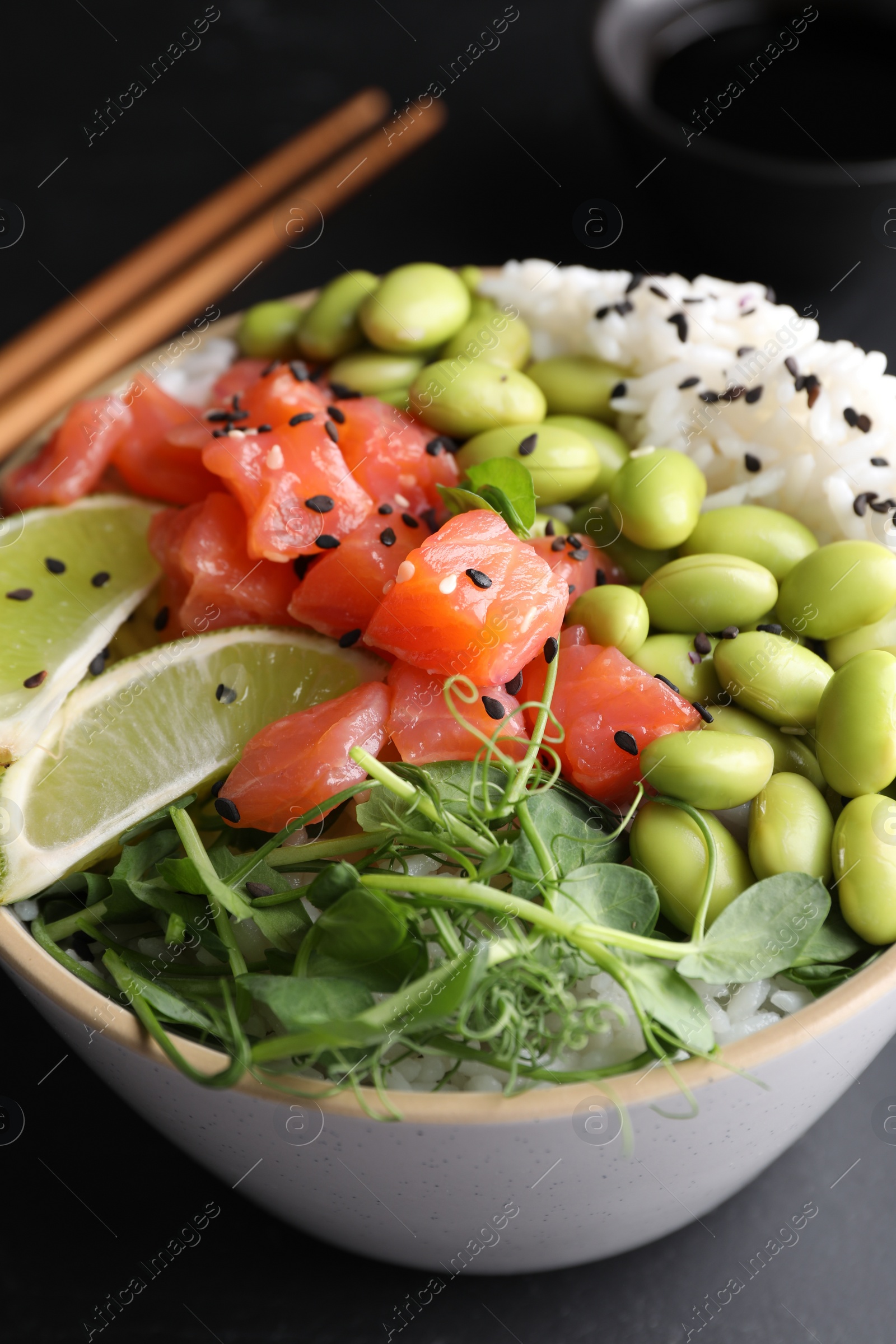 Photo of Delicious poke bowl with lime, fish and edamame beans on black table, closeup