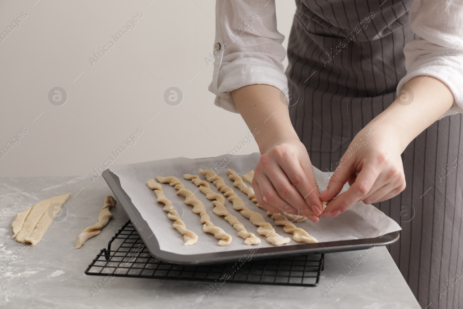 Photo of Woman putting homemade breadsticks on baking sheet at light grey marble table, closeup. Cooking traditional grissini