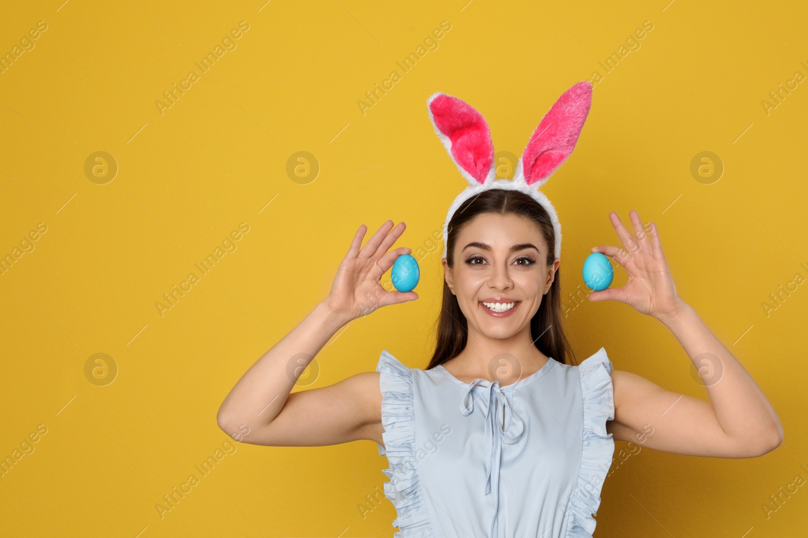 Photo of Beautiful woman in bunny ears headband holding Easter eggs on color background, space for text