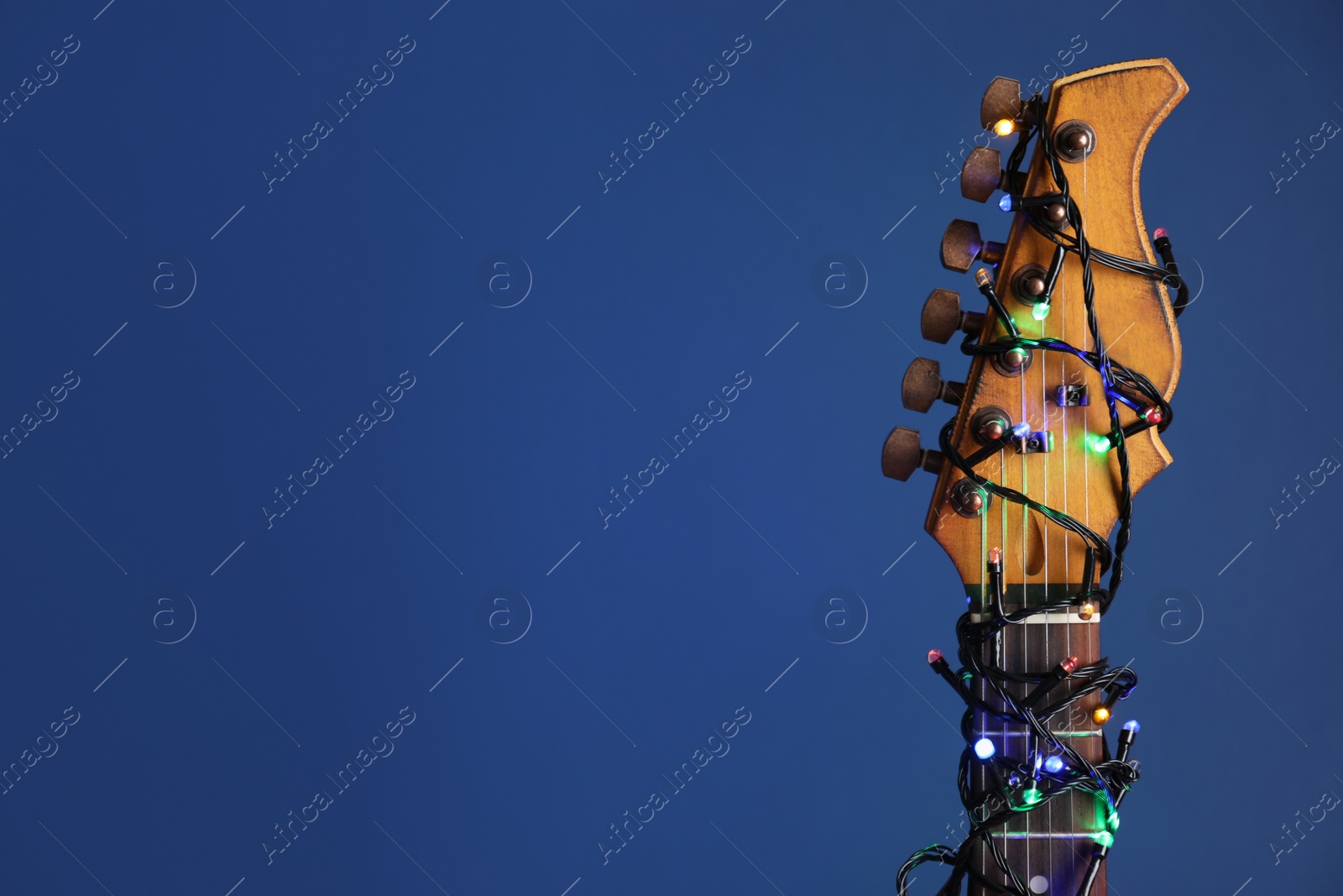Photo of Guitar with festive lights on blue background, space for text. Christmas music