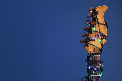 Photo of Guitar with festive lights on blue background, space for text. Christmas music