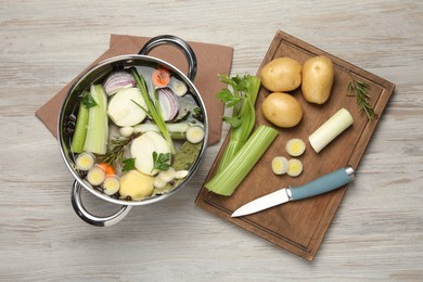 Pot and different ingredients for cooking tasty bouillon on white wooden table, flat lay