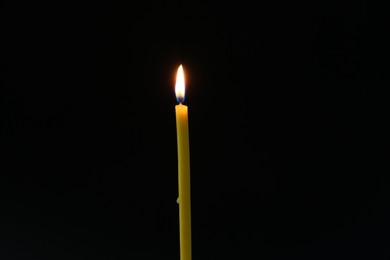 Photo of One burning church candle on dark background