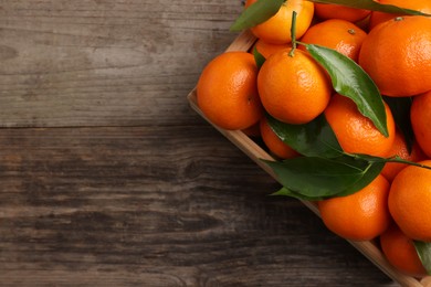 Delicious tangerines with leaves on wooden table, top view. Space for text