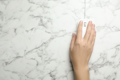 Woman using wired computer mouse on marble table, top view. Space for text