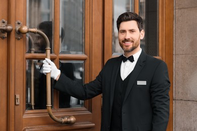 Photo of Butler in elegant suit and white gloves opening wooden hotel door