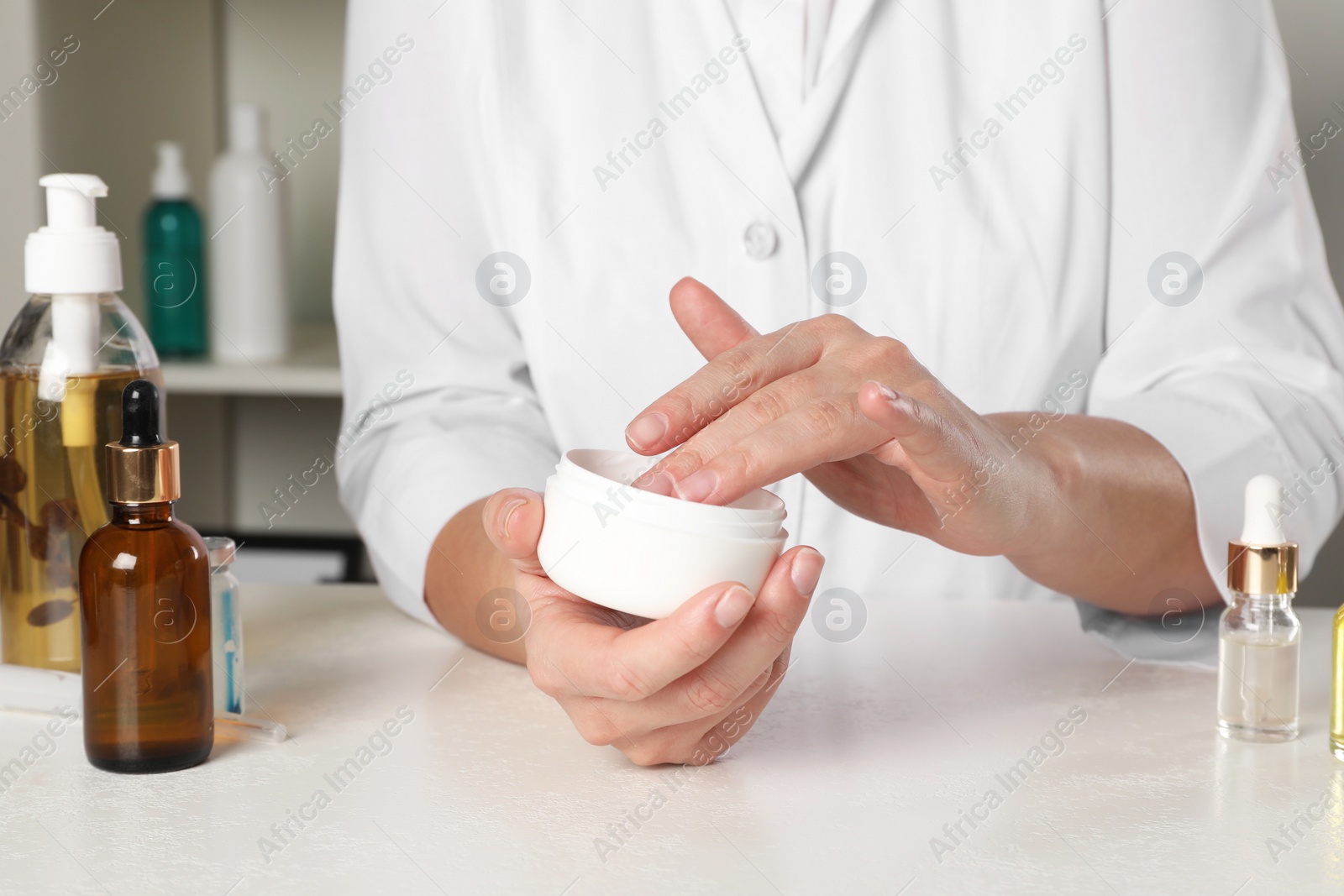 Photo of Dermatologist testing cosmetic product at white table indoors, closeup