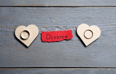 Paper sheet with word Divorce and wedding rings on grey wooden table, flat lay