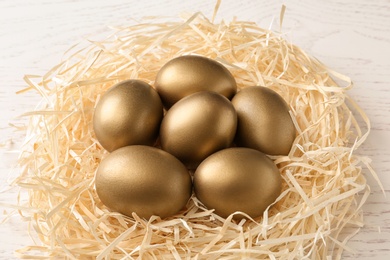Golden eggs in nest on wooden background