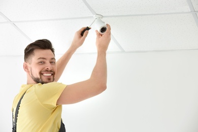 Photo of Technician installing CCTV camera on ceiling indoors