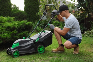 Young man fixing lawn mower in garden