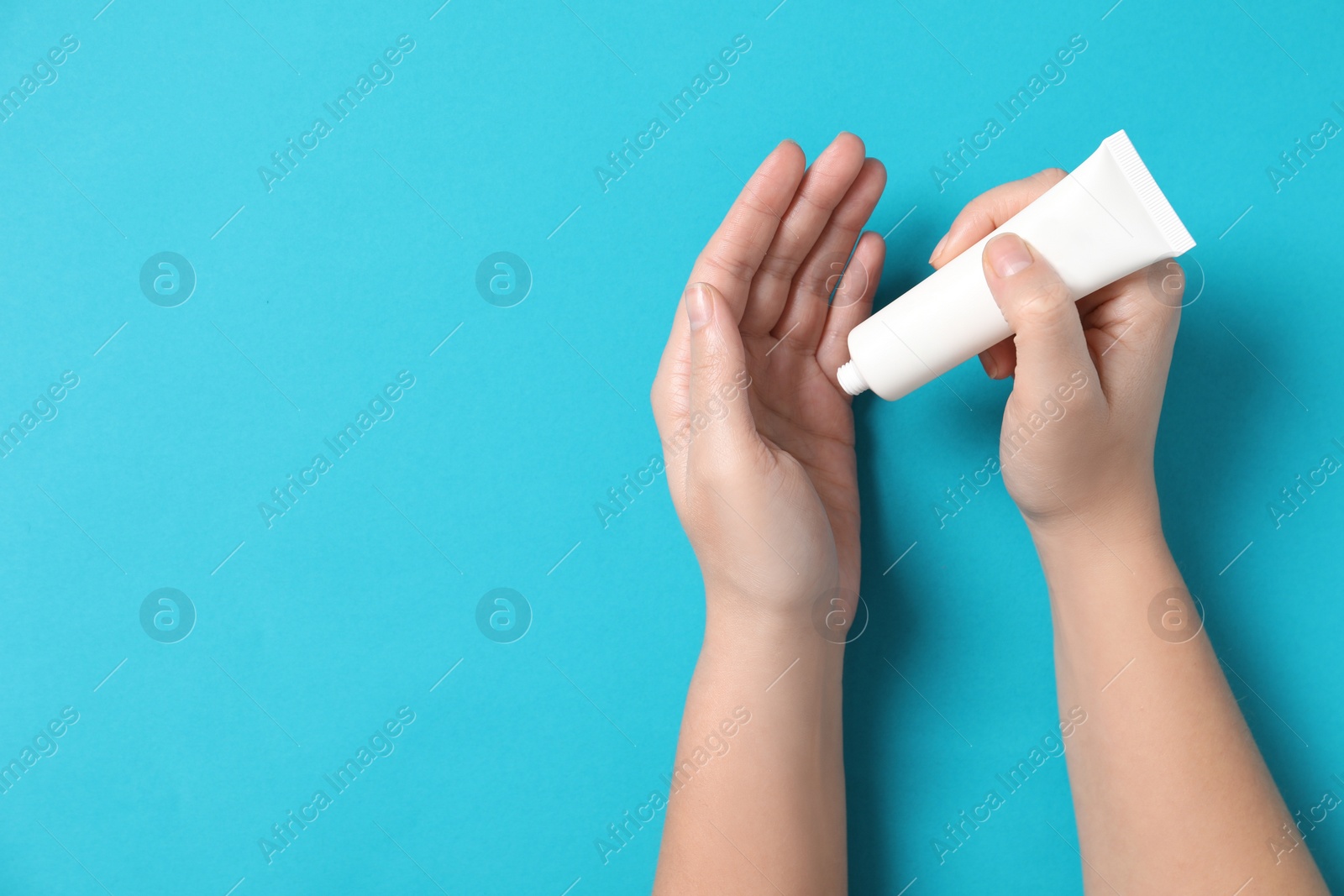 Photo of Woman applying cosmetic cream from tube onto her hand on light blue background, top view. Space for text