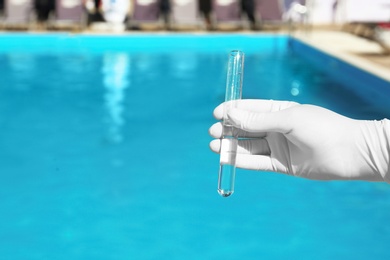 Photo of Woman holding glass tube with sample of swimming pool water to check PH level outdoors, closeup