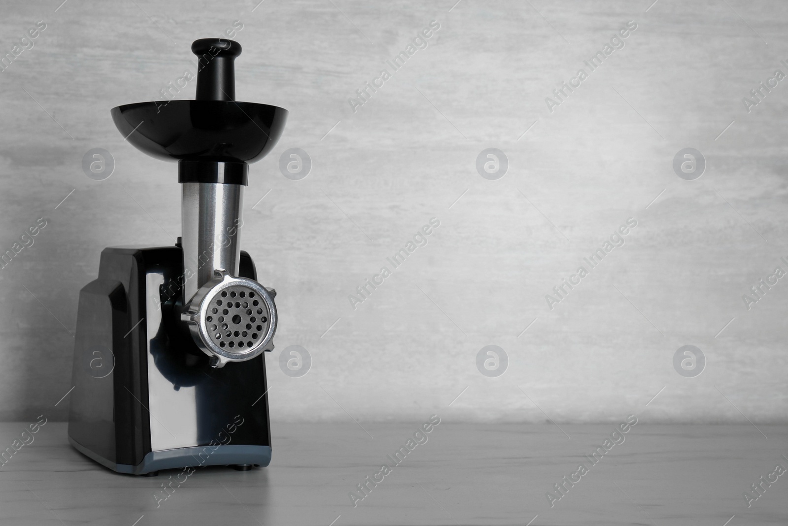 Photo of Modern electric meat grinder on light wooden table. Space for text