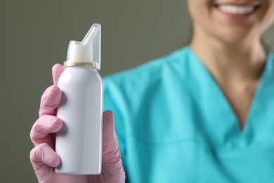 Photo of Woman holding nasal spray bottle on olive background, closeup. Space for text