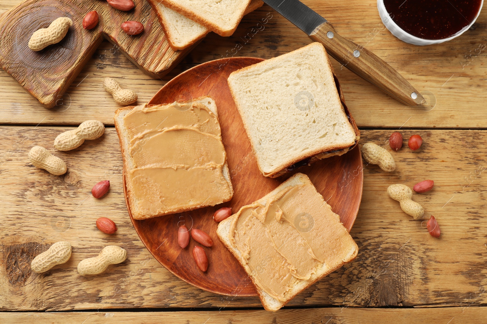 Photo of Tasty peanut butter sandwiches and peanuts on wooden table, flat lay