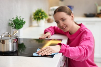 Photo of Woman cleaning electric stove with rag in kitchen, selective focus