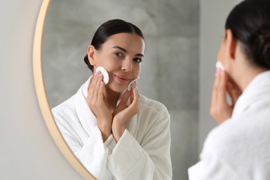 Photo of Beautiful woman removing makeup with cotton pads near mirror indoors