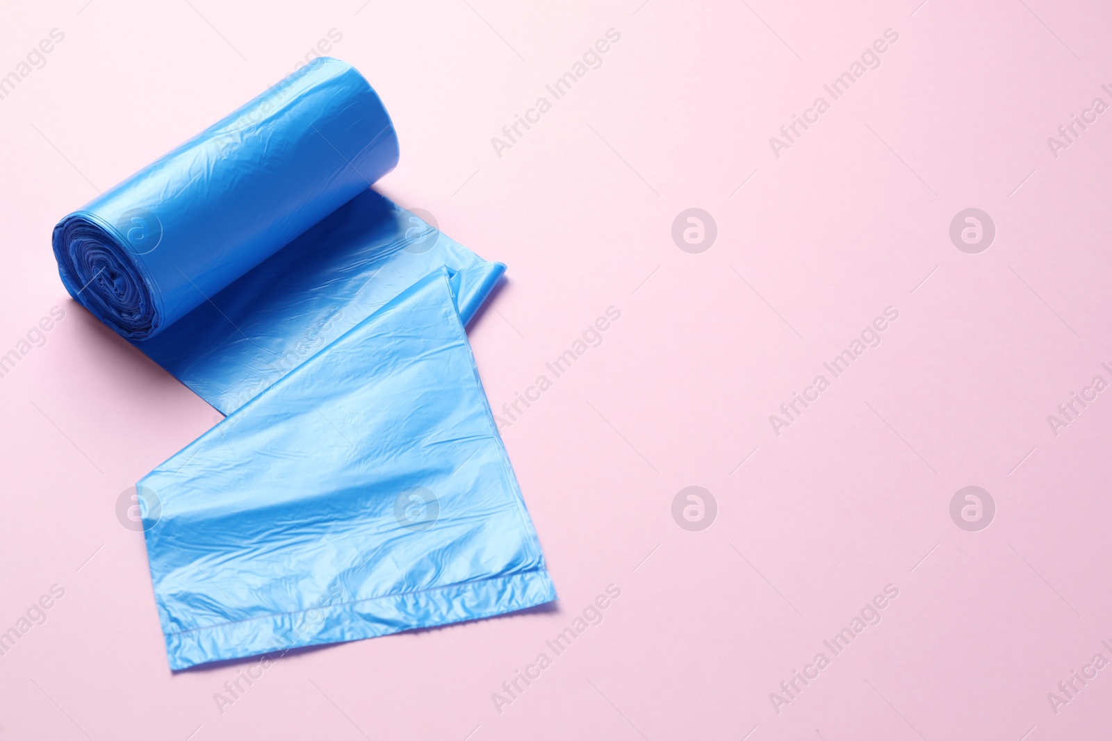 Photo of Roll of turquoise garbage bags on pink background, space for text. Cleaning supplies