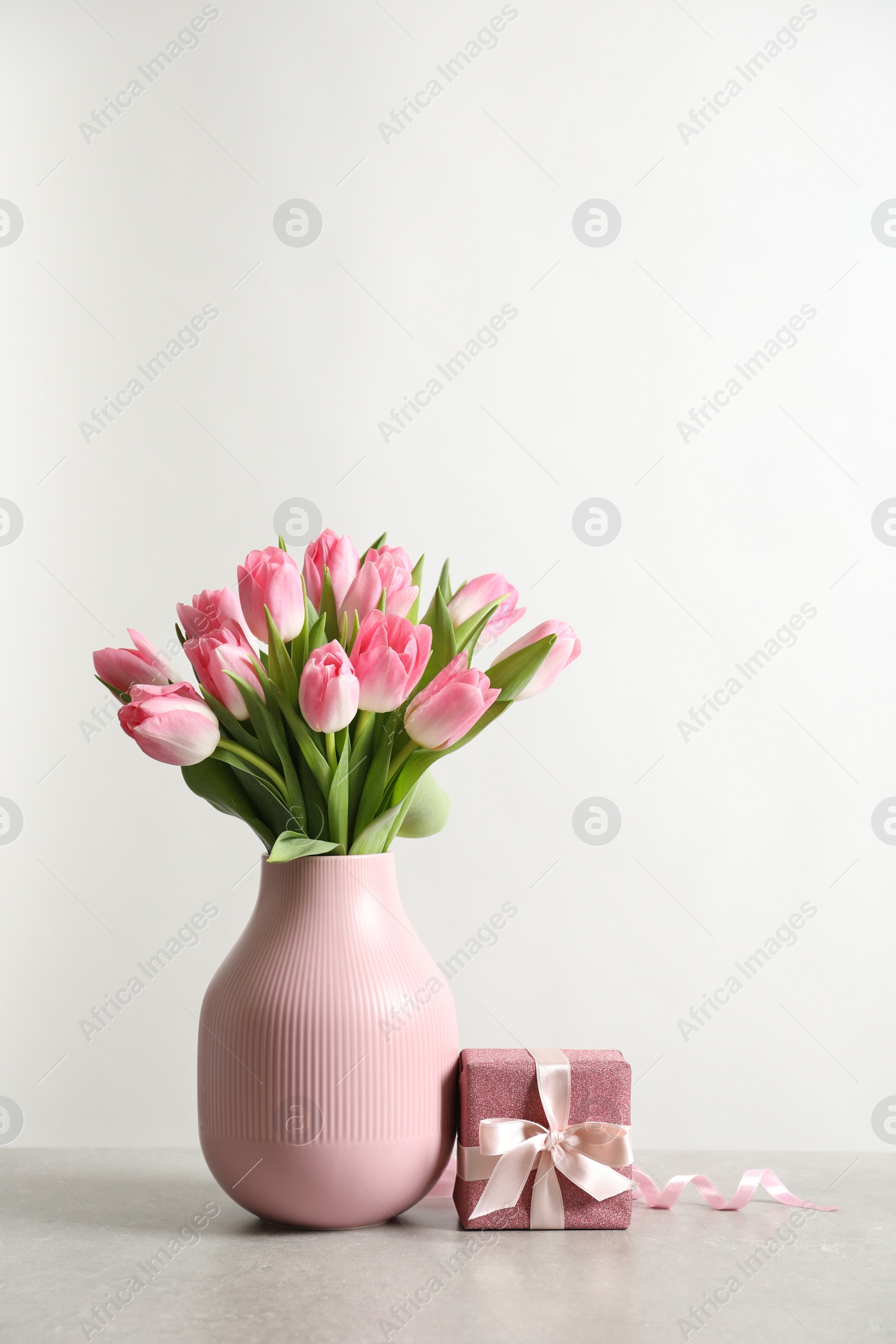 Photo of Bouquet of beautiful spring tulips in vase and gift box on table against white background. International Women's Day