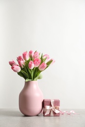 Bouquet of beautiful spring tulips in vase and gift box on table against white background. International Women's Day